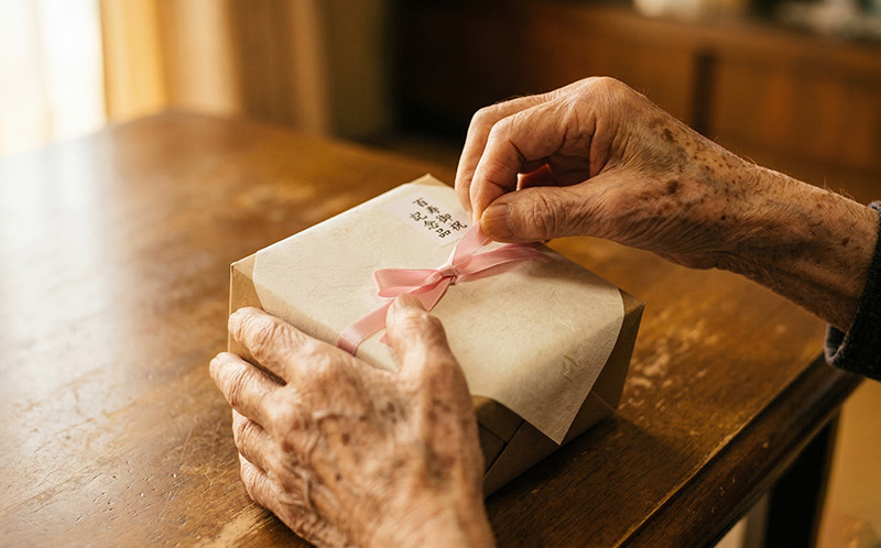 ピンクのリボンのギフトを丁寧に開ける高齢者の手元