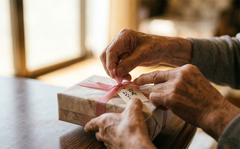 ピンクのリボンのギフトを丁寧に開ける100歳の手元クローズアップ