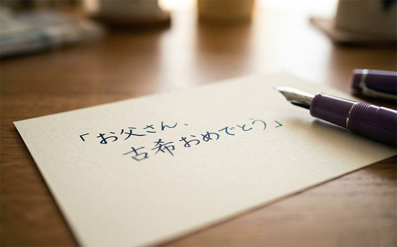 「お父さん、古希おめでとう」と書かれた手書きの手紙と紫の万年筆