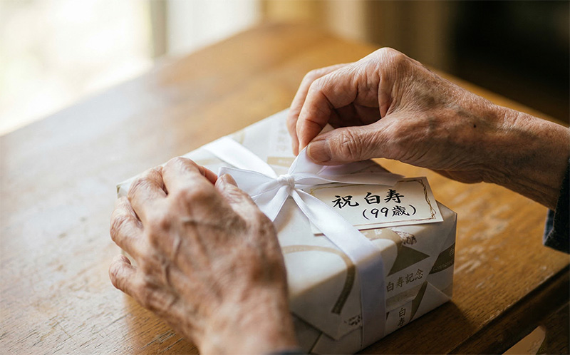 白いリボンの白寿祝いギフトを丁寧に開ける99歳の手元