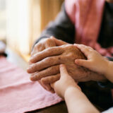 100歳の祖父の手と孫の小さな手が優しく重なるピンクの布の上