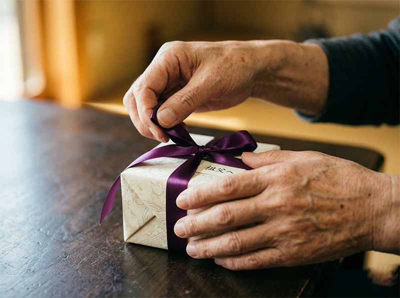 紫のリボンがかかったプレゼントを開ける高齢者の手元