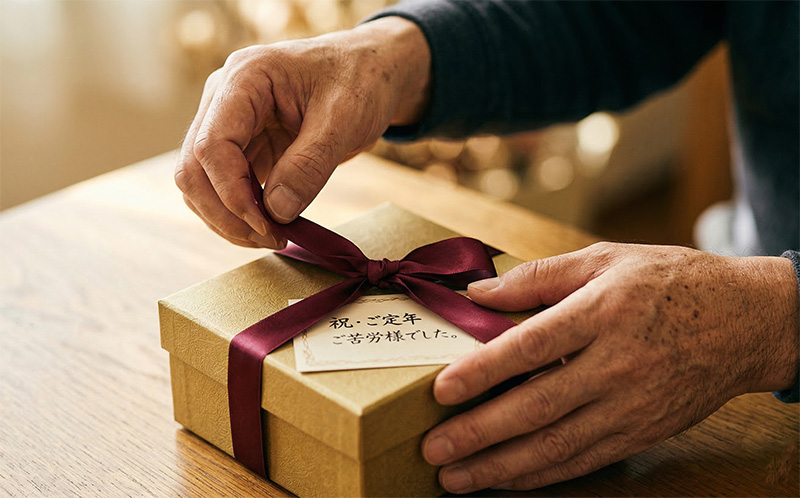 退職祝いのギフトのリボンをほどく60代男性の手元接写