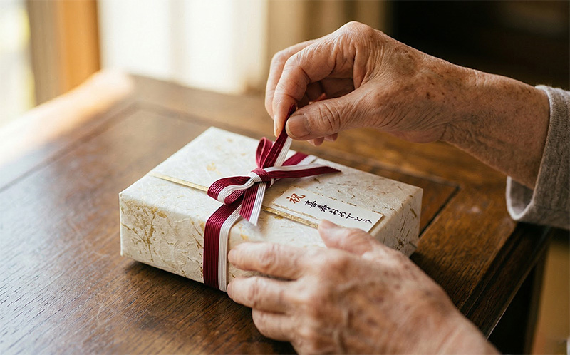 長寿祝いのギフトのリボンを丁寧にほどく高齢者の手元