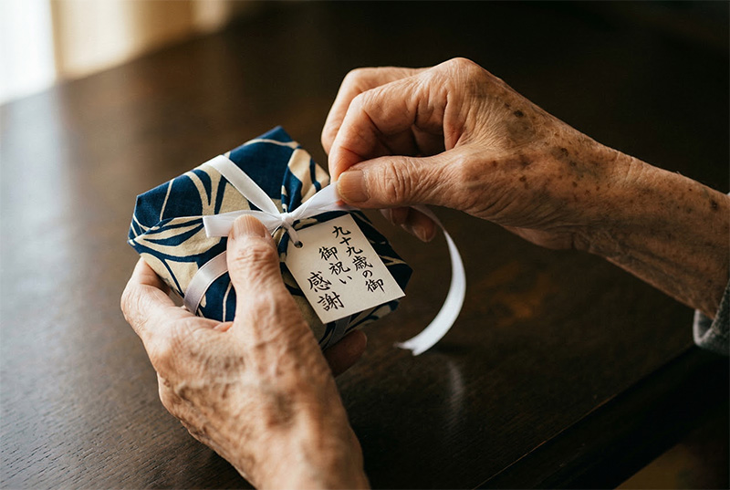 白いリボンの贈り物を丁寧に開ける99歳の手元クローズアップ