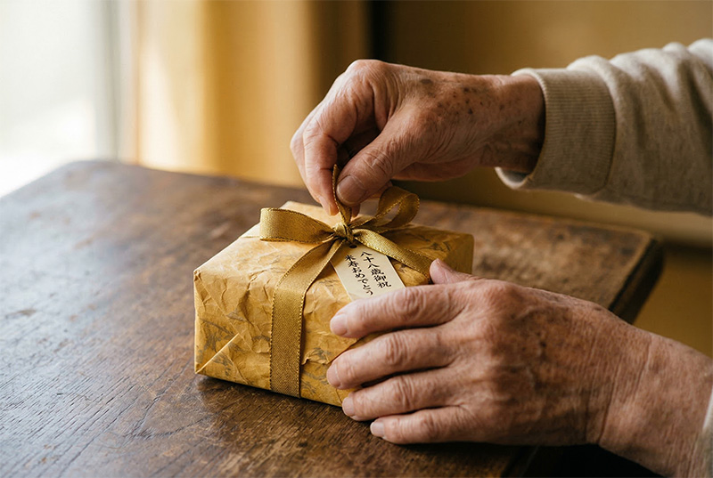 金リボンのギフトを丁寧に開ける88歳の手元クローズアップ