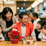 赤いちゃんちゃんこを着た60歳男性と家族に囲まれた還暦祝い